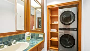 A bathroom with a sink, mirror, and wooden shelving unit containing a washing machine and dryer.