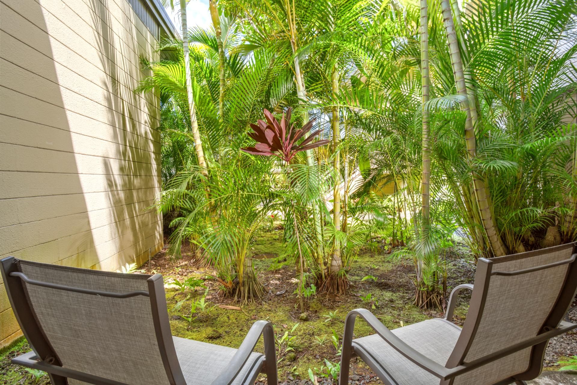 A patio with two chairs and lush tropical plants.