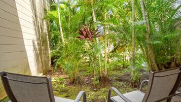 A patio with two chairs and lush tropical plants.
