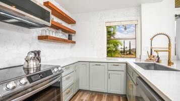 A modern kitchen with a built-in stove, stainless steel kettle, and wooden shelves.