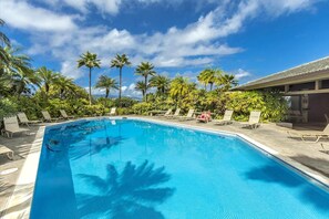 Una piscina con sillones de descanso y palmeras.