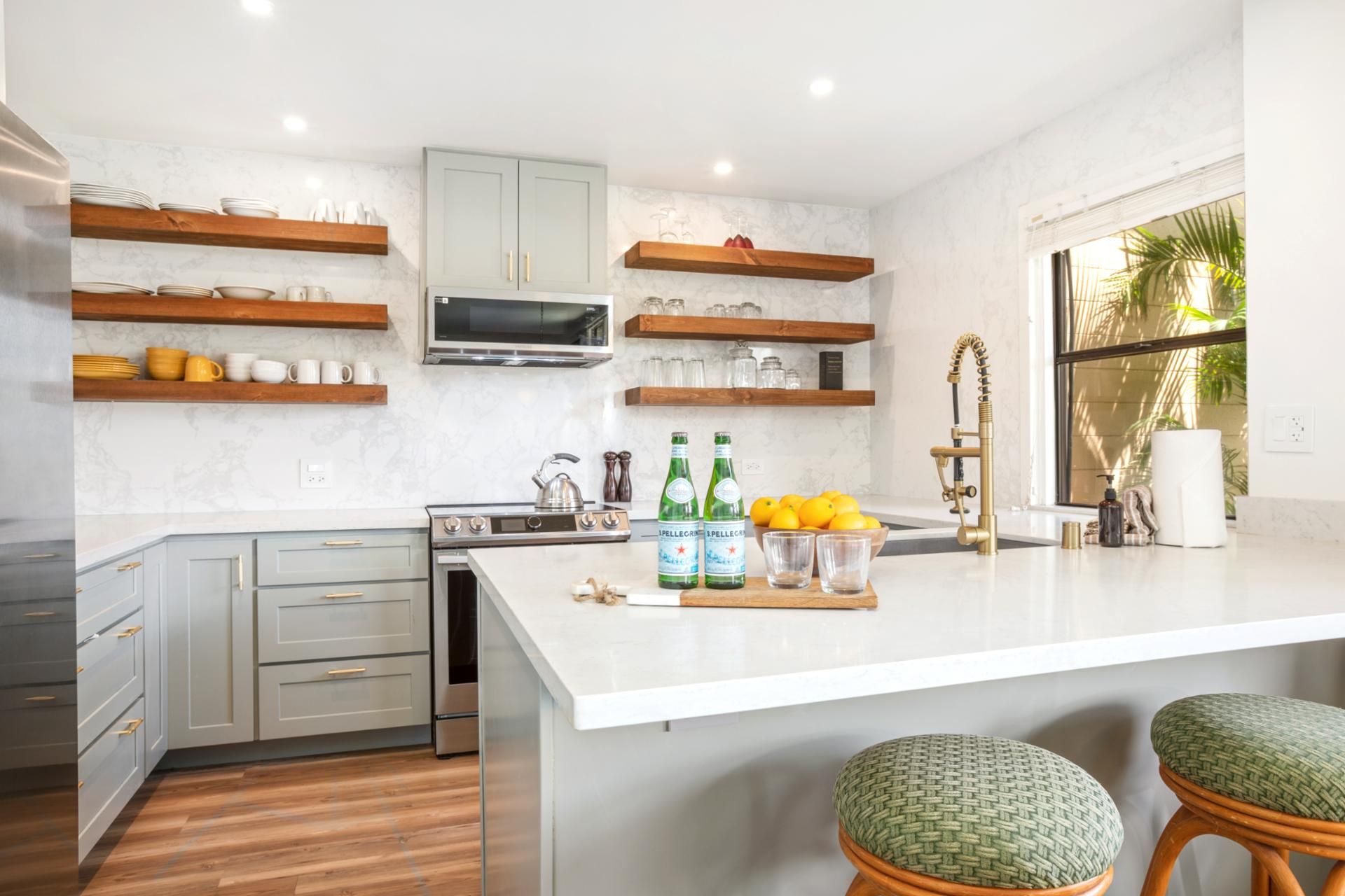 A modern kitchen with grey cabinets, wooden shelves, a built-in oven, and a large island with stools.