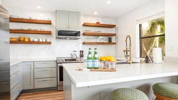 A modern kitchen with grey cabinets, wooden shelves, a built-in oven, and a large island with stools.