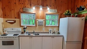 A kitchen with wooden walls, a white stove, a sink, and a refrigerator. - Gowdas Cottage (New Glasgow)