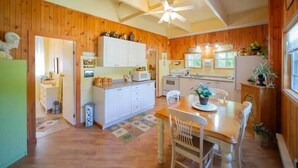 A kitchen with wooden walls, white cabinets, a dining table with chairs, and a ceiling fan. - Gowdas Cottage (New Glasgow)