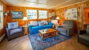 A cozy room with wooden walls, a blue sofa, a grey armchair, and a wooden coffee table. - Gowdas Cottage (New Glasgow)