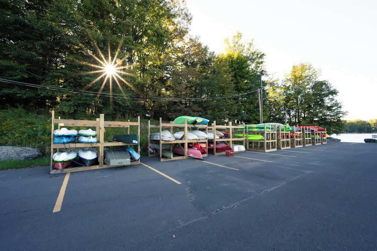 A parking area with rows of kayaks and canoes stored on wooden racks.