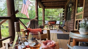 Une terrasse en bois avec des sièges d’extérieur, une bouteille de vin et un verre de vin posés sur une table.