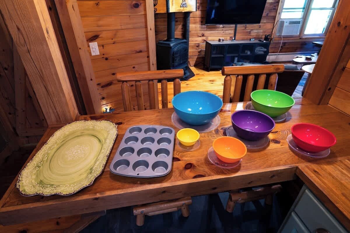 A wooden dining table with colorful bowls, a decorative plate, and a muffin tray.