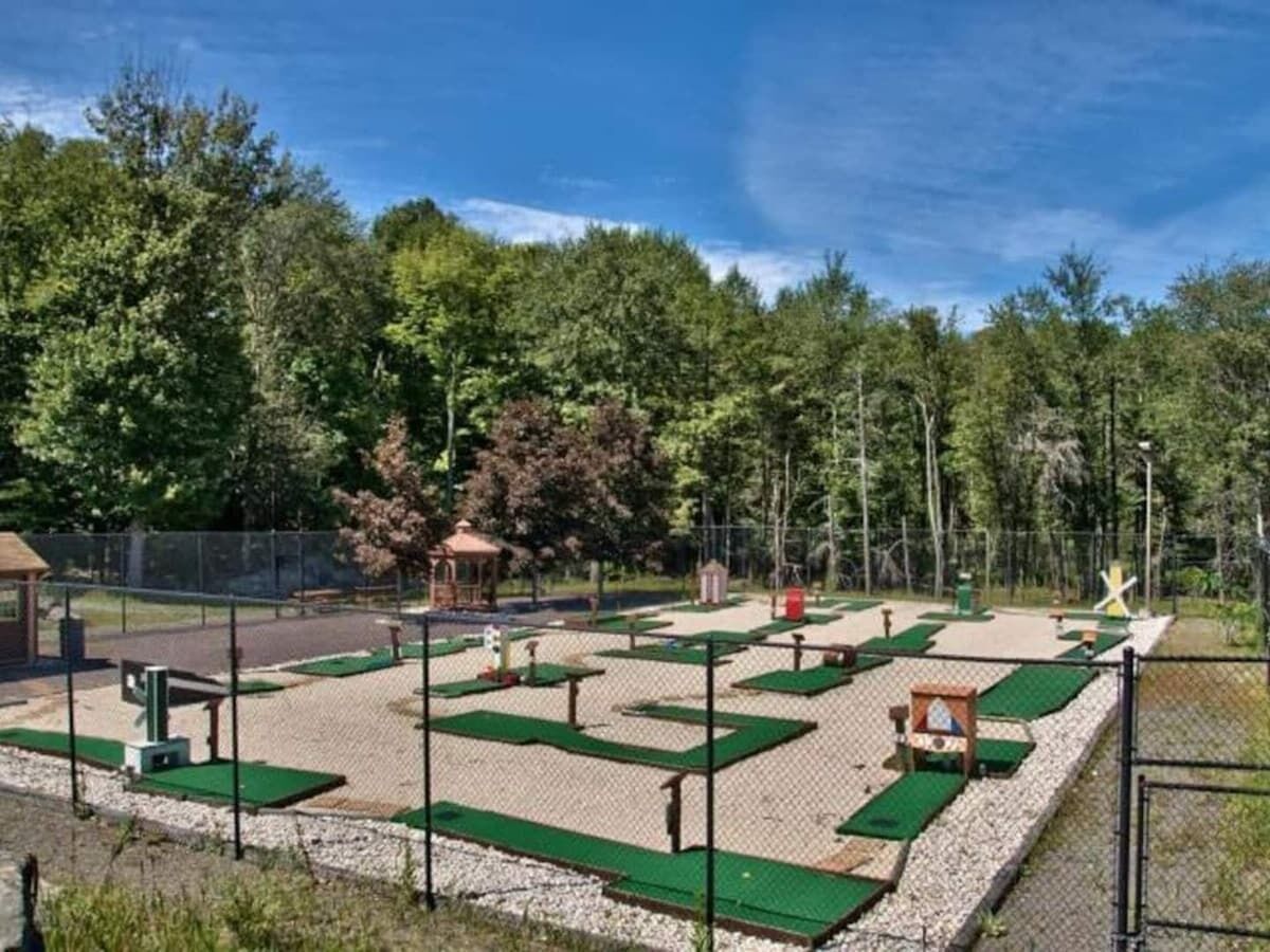 An outdoor golf driving range with multiple green tee boxes and a fenced area.