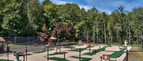 An outdoor golf driving range with multiple green tee boxes and a fenced area.