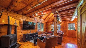 L’intérieur d’une cabane en rondins, avec une cheminée, un canapé et un téléviseur.