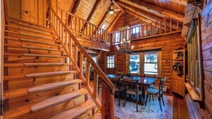 L'intérieur d'un chalet en bois, avec un escalier, un coin repas et de grandes fenêtres.