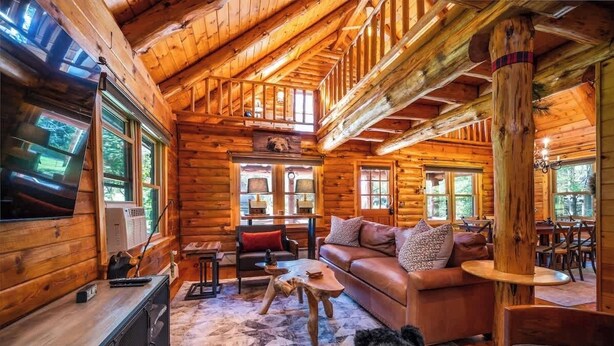 L’intérieur d’une cabane en rondins présente un espace de vie chaleureux, avec un canapé, une table basse et une cheminée.