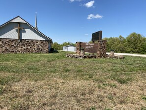 A stone building with a cross on the roof, a sign reading "RIDGE CHAPEL," and a stone structure with a cross in front.