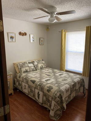 A bedroom with a bed, a ceiling fan, a window with curtains, and wall decorations.