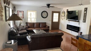 A living room with a brown leather sofa, a coffee table, a TV, and a dining area with a bar counter. - A place to unwind!! (Kansas)