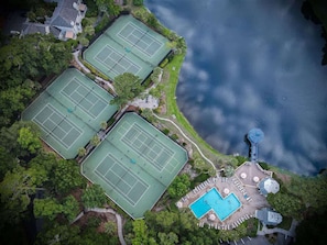 An aerial view of a property with multiple tennis courts, a swimming pool, and a dock.