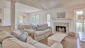 A spacious living room with a fireplace, a dining area with wicker chairs, and a large window providing natural light.