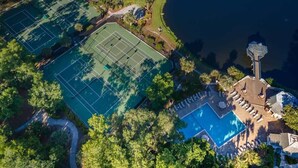 An aerial view of a property with multiple tennis courts, a swimming pool, and a tower structure.