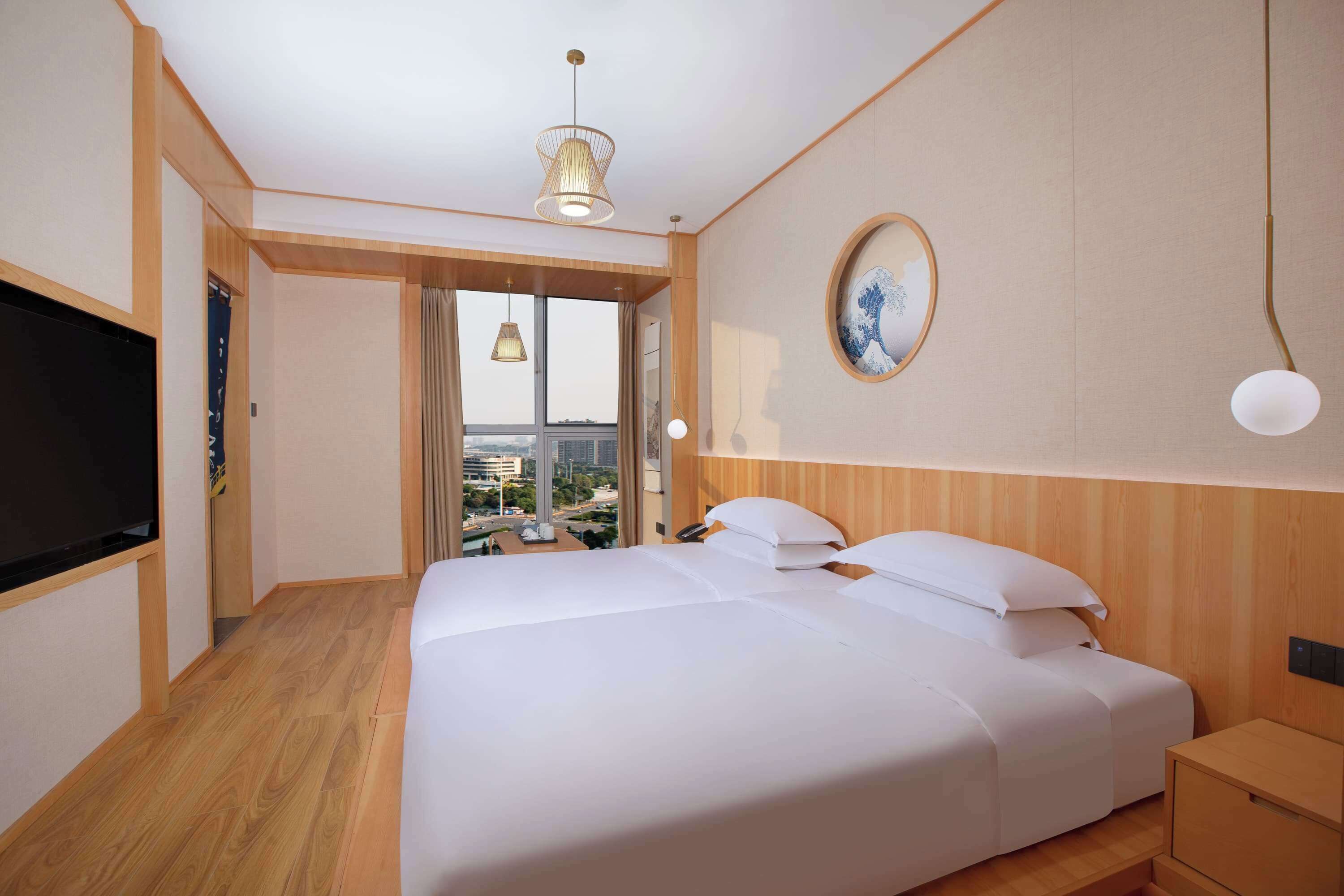 Een moderne hotelkamer met een groot bed, houten vloeren, een televisie en uitzicht op de stad.