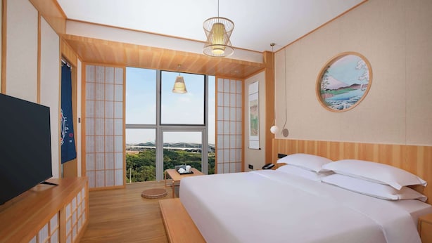 A hotel room with a large bed, a TV, a desk, and a view of greenery through large windows. - Days Hotel by Wyndham Changsha South (Changsha)