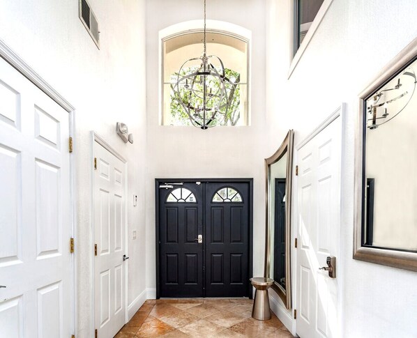 A hallway with two black doors, a large mirror, and a chandelier.
