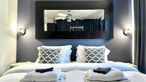 Habitación de hotel con una cama grande, dos almohadas, un ventilador de techo y un espejo en la pared.