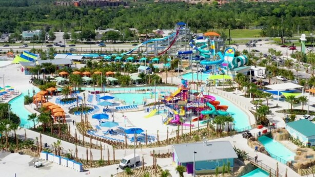 Parque acuático con múltiples toboganes y piscinas, rodeado de palmeras y un estacionamiento.