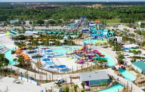 A water park with multiple slides and pools, surrounded by palm trees and a parking area.