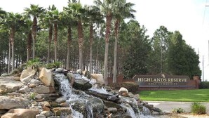 Una cascada, palmeras y un letrero del complejo residencial Highlands Reserve Golf Community.