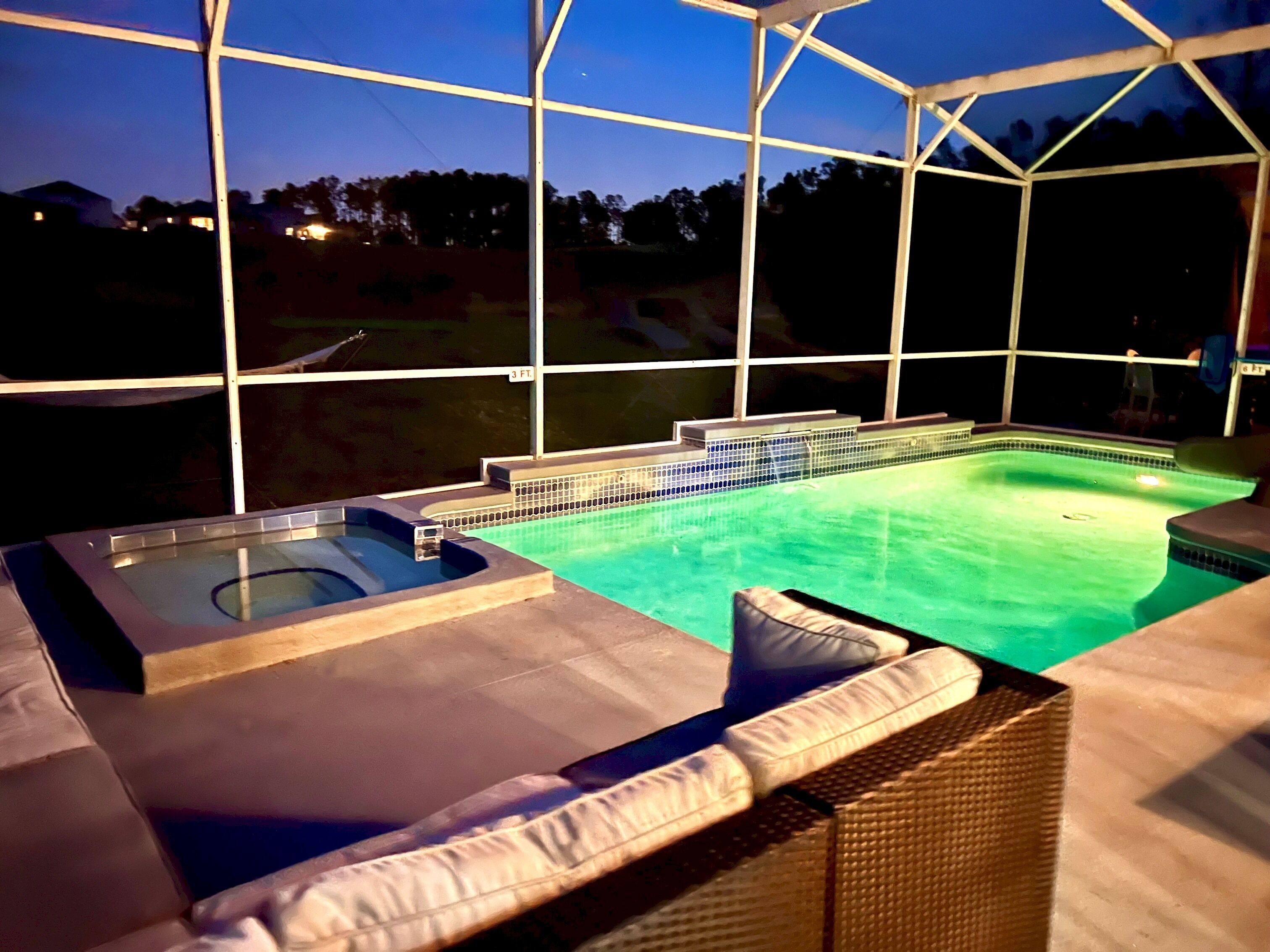 A covered outdoor swimming pool with a hot tub, lounge chairs, and a view of the surrounding area.