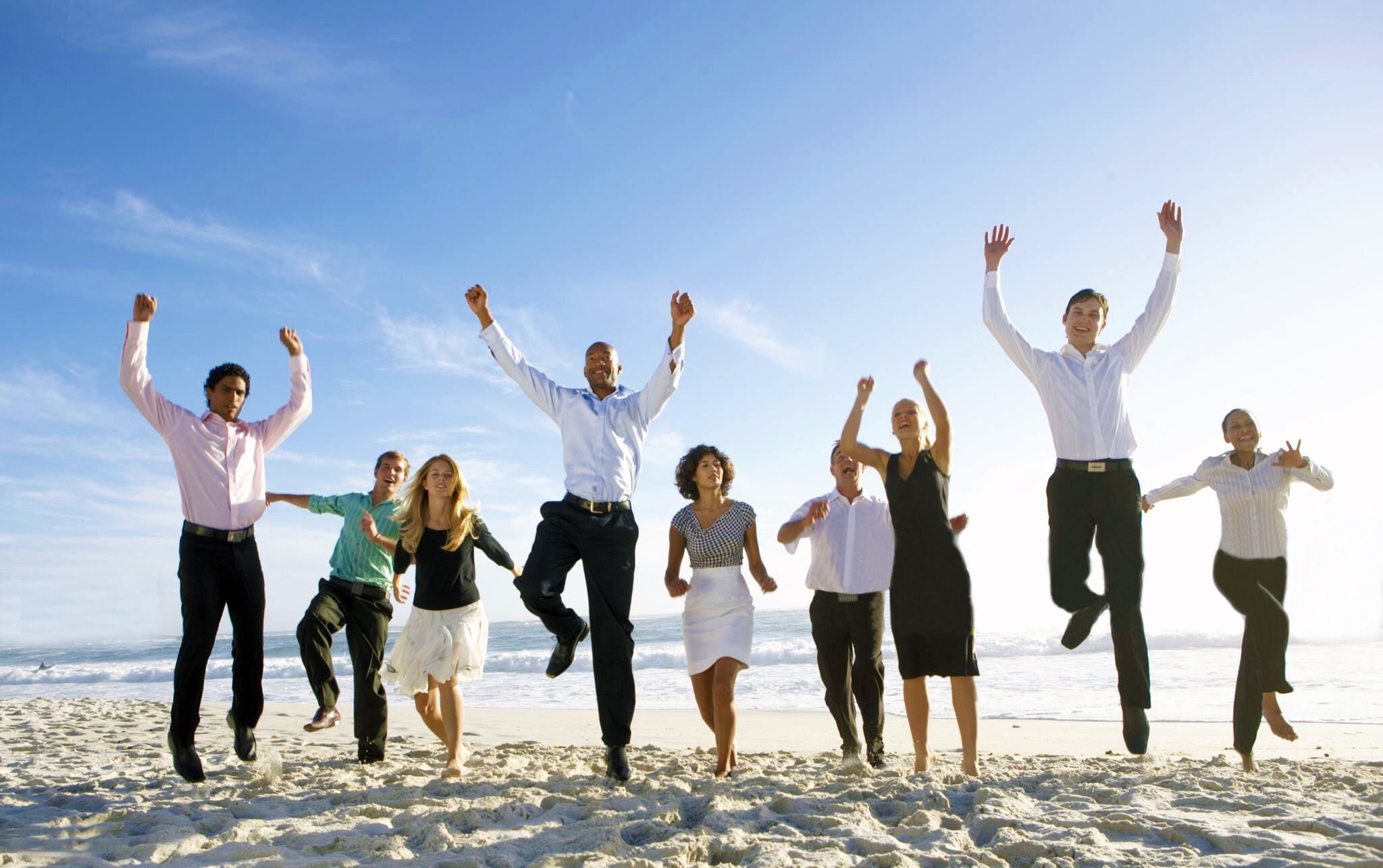 A group of people jumping on a beach with the ocean in the background.