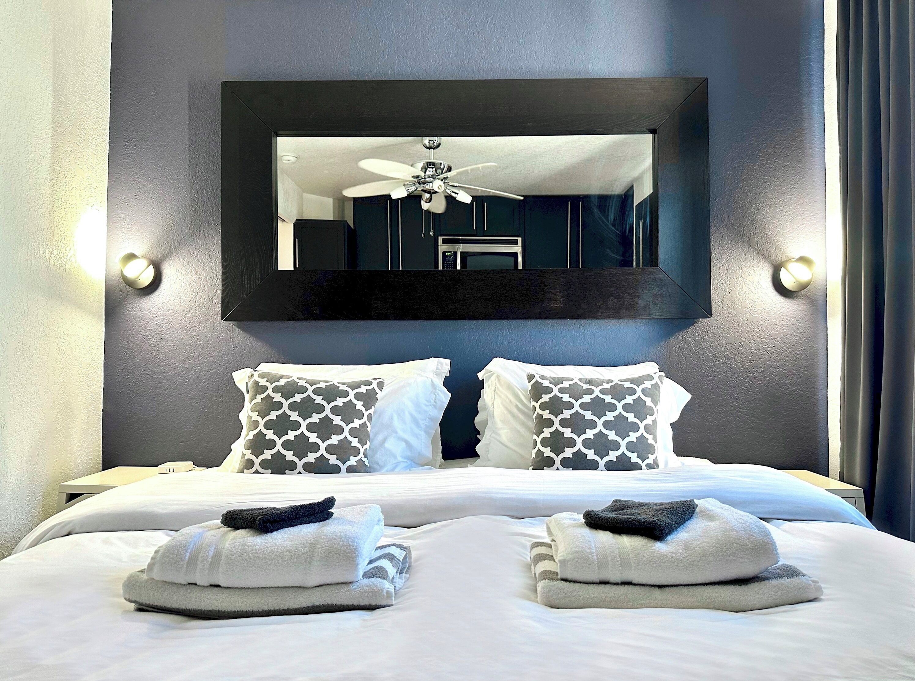 A hotel room with a large bed, two pillows, a ceiling fan, and a mirror on the wall.