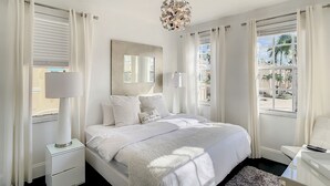 Une chambre à coucher moderne avec un grand lit, des lampes de chevet, un lustre et une vue sur l’extérieur.