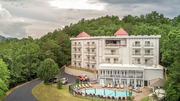 Un hotel de varios pisos con zona de piscina, rodeado de exuberante vegetación y un camino sinuoso.