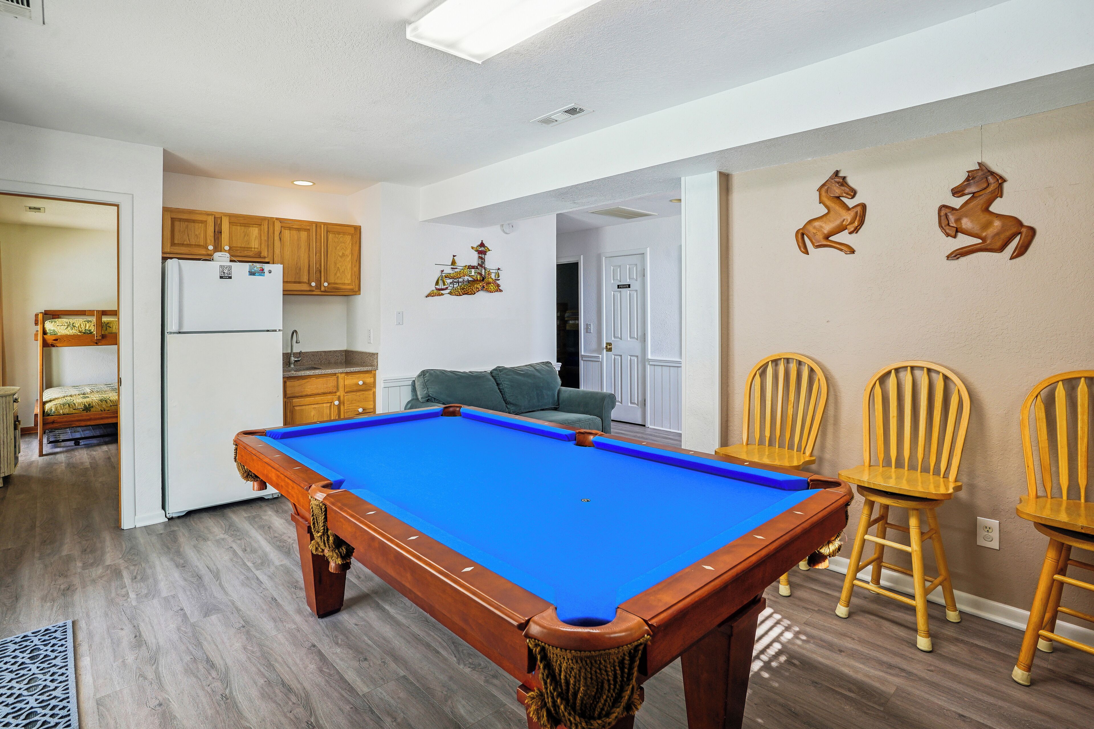 A pool table in a room with wooden cabinets, a sofa, and two wooden chairs.
