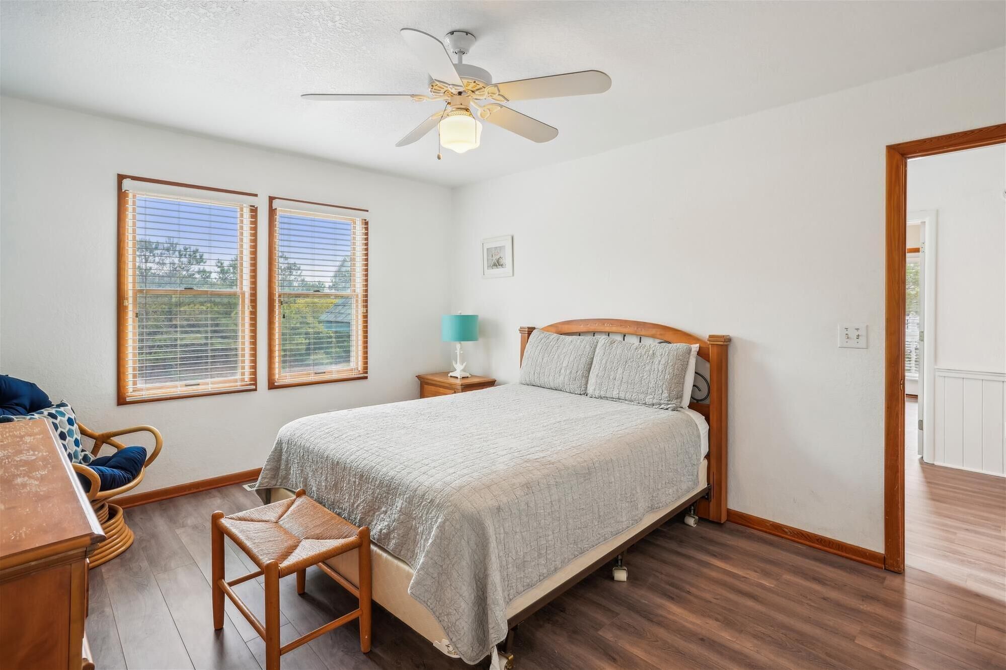 A bedroom with a bed, a chair, a desk, a ceiling fan, and two windows.