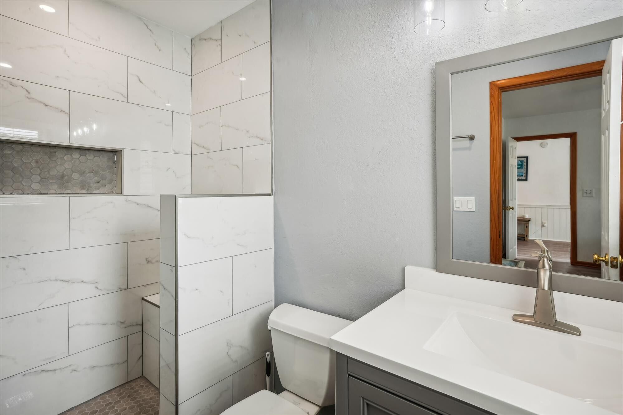 A bathroom with white marble tiles, a white sink with a modern faucet, and a mirror with a wooden frame.