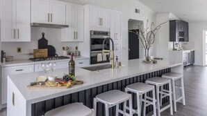 A modern kitchen with white cabinetry, a central island with stools, a built-in oven, and a stainless steel range. - Old Town Fashioned-Pool-Putting Green-BBQ Grill (Scottsdale)