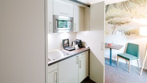 A compact kitchenette with a microwave, coffee maker, and a small table with a chair. - Hotel Am Zoo (Neunkirchen)