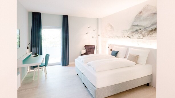 A modern hotel room with a large bed, a desk, and a chair. - Hotel Am Zoo (Neunkirchen)