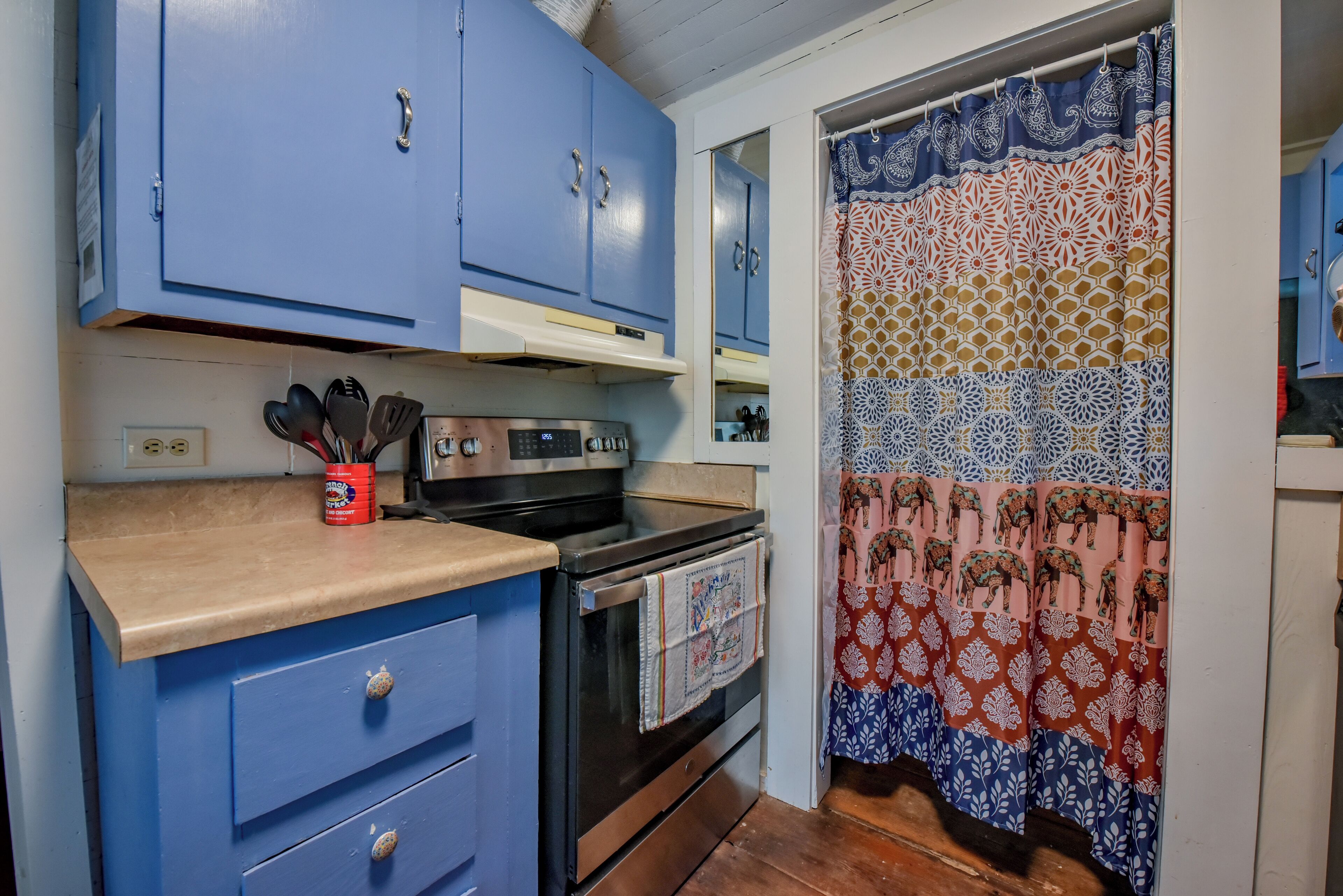 A kitchen with blue cabinets, a stove, and a patterned curtain.