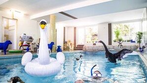 An indoor swimming pool with inflatable swan and duck floats, a large column, and a view of the outside through large windows.