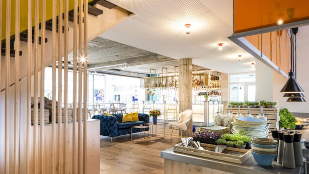 A modern interior with a bar area, wooden flooring, and a blue sofa with yellow cushions.