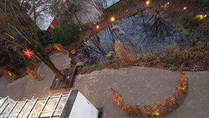A circular garden area with a stone pathway, surrounded by trees and a small pond.