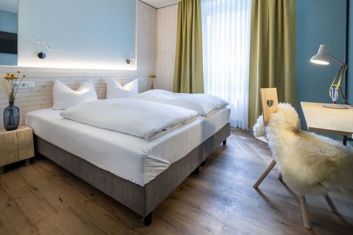 Quarto moderno com uma cama grande, mesas de cabeceira, escrivaninha e uma cadeira.