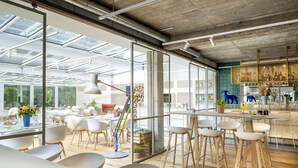 A modern interior with large windows, wooden flooring, and a mix of white and wooden chairs.
