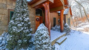 A wooden house with a covered porch, snow-covered trees, and a stone staircase leading to the entrance. - Buckhorn Lodge - Spacious Luxury Home Near Sugar Mountain Resort, Pool Table, Hot Tub, Views (Sugar Mountain)