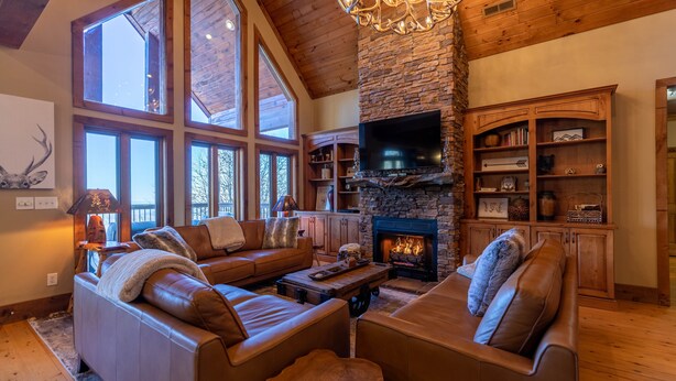 A cozy living room with a stone fireplace, leather sofas, and a large TV. - Buckhorn Lodge - Spacious Luxury Home Near Sugar Mountain Resort, Pool Table, Hot Tub, Views (Sugar Mountain)